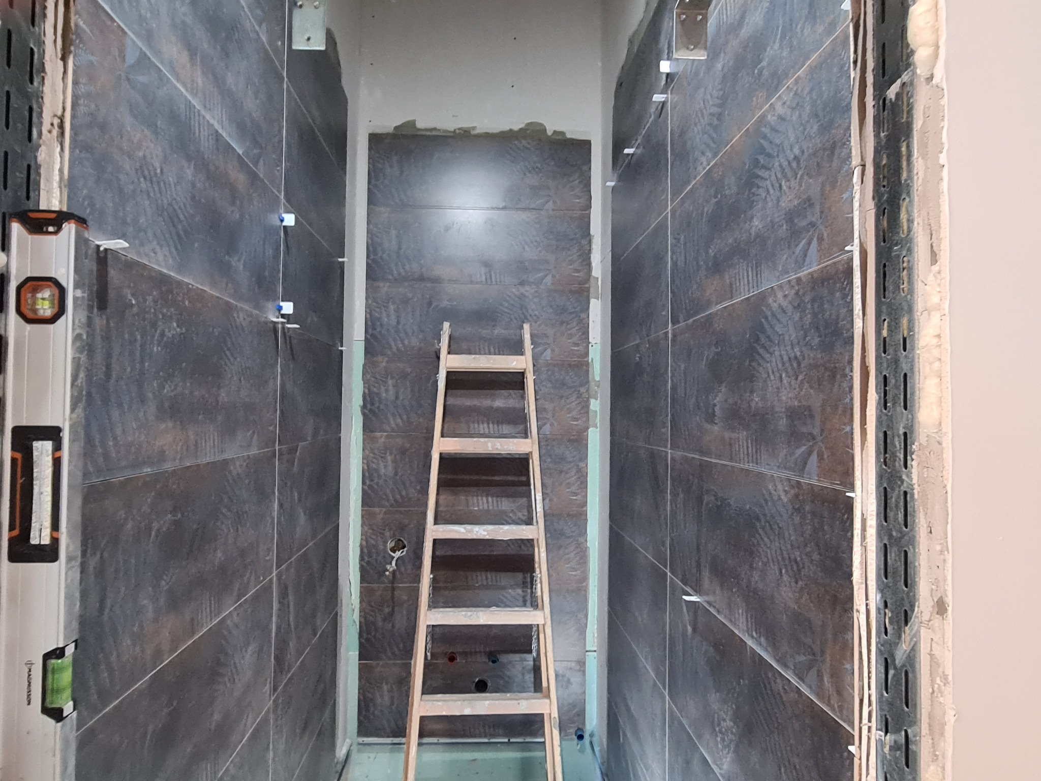 Wnętrze łazienki w trakcie układania płytek imitujących drewno, widoczna drabina, poziomica przy ścianie, system poziomowania płytek.