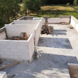 Michał Leszkowski - Wznoszenie ścian parteru domu z bloczków betonu komórkowego, widok z góry na budowę w słoneczny dzień, drewniane deski leżące na stropie.