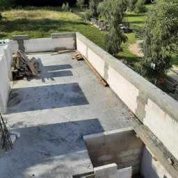 Michał Leszkowski - Wznoszenie ścian domu z betonu komórkowego, widok z góry na surowy stan z zaznaczonym wejściem do piwnicy, w tle zielony krajobraz.