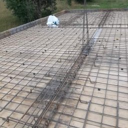 Michał Leszkowski - Zbrojenie płyty fundamentowej z widocznymi prętami pionowymi i workiem z materiałem budowlanym w tle.