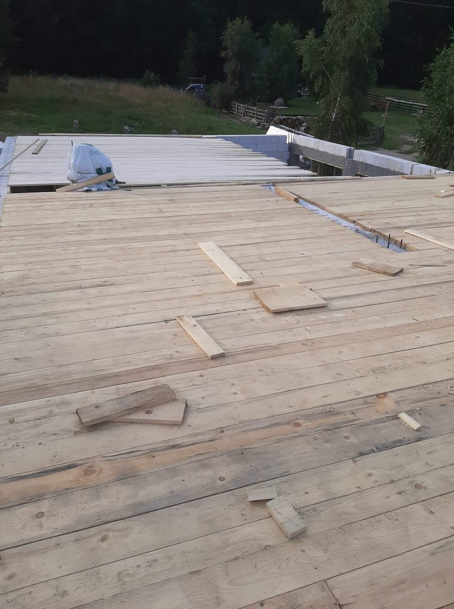 Drewniany szalunek stropu w trakcie budowy, widoczne wystające pręty zbrojeniowe i białe bloczki silikatowe na obrzeżach, w tle zalesiony teren.