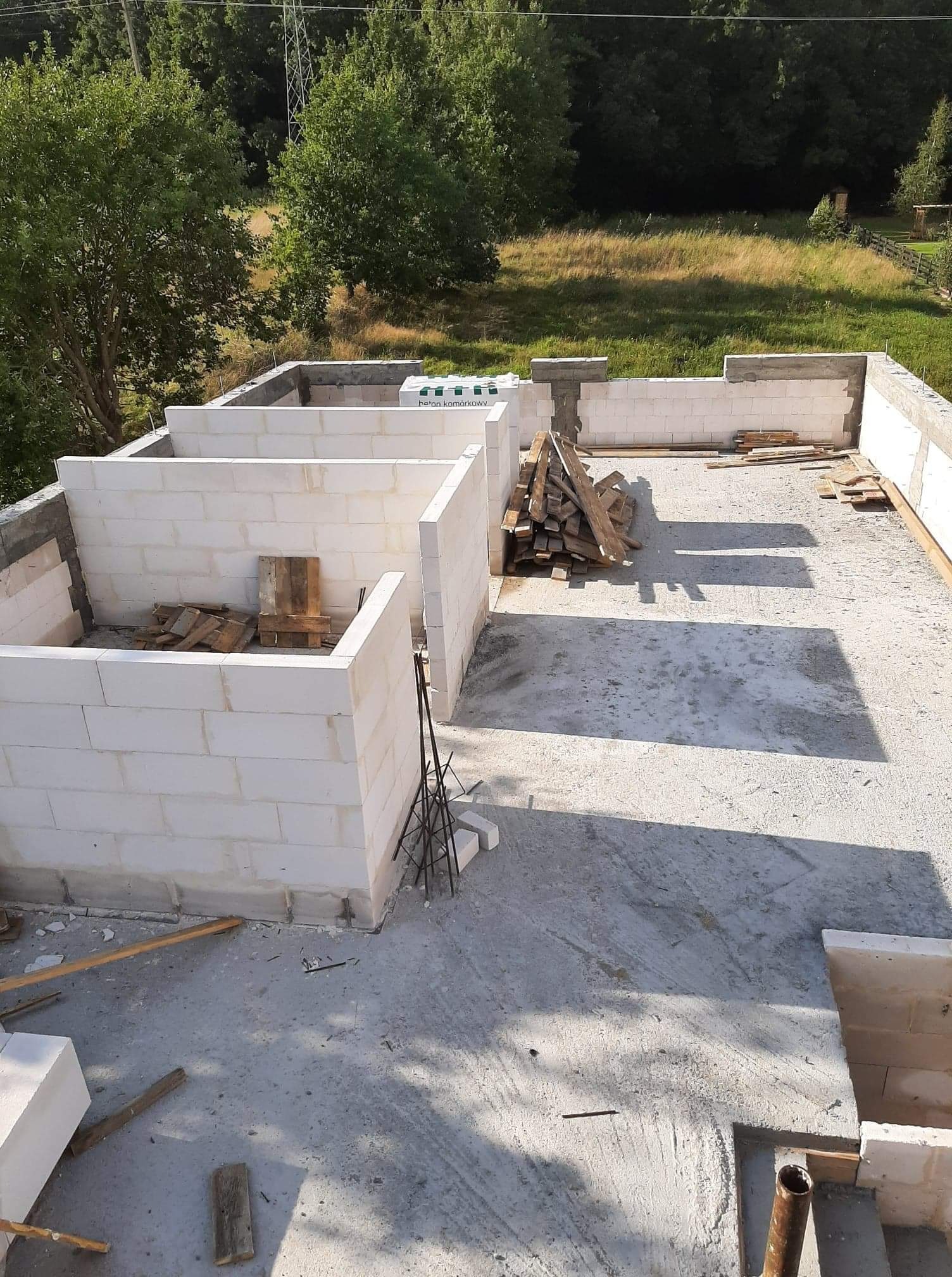 Wznoszenie ścian parteru domu z bloczków betonu komórkowego, widok z góry na budowę w słoneczny dzień, drewniane deski leżące na stropie.