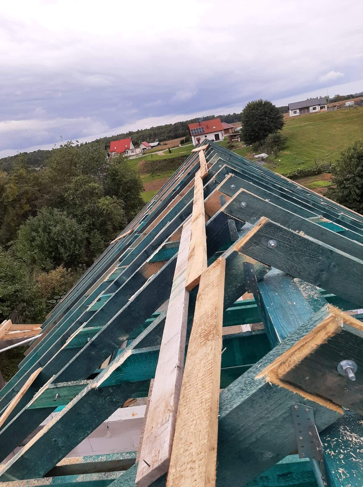 Konstrukcja dachu z impregnowanego drewna, widok z góry na tle zieleni i zabudowań.