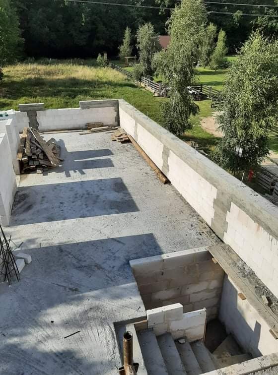 Wznoszenie ścian domu z betonu komórkowego, widok z góry na surowy stan z zaznaczonym wejściem do piwnicy, w tle zielony krajobraz.