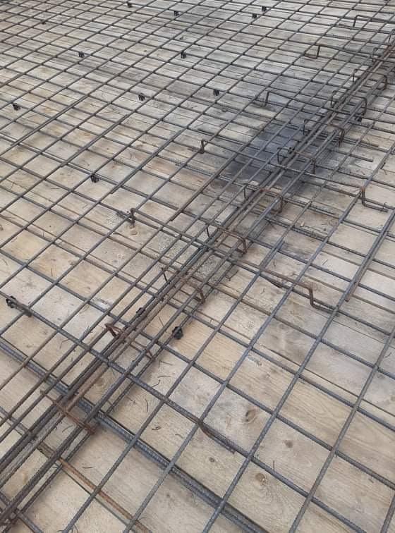 Zbrojenie fundamentu w postaci siatki z prętów stalowych, z zachowaniem dystansu od podłoża za pomocą plastikowych podkładek dystansowych, widok z góry.