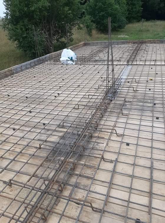 Zbrojenie płyty fundamentowej z widocznymi prętami pionowymi i workiem z materiałem budowlanym w tle.