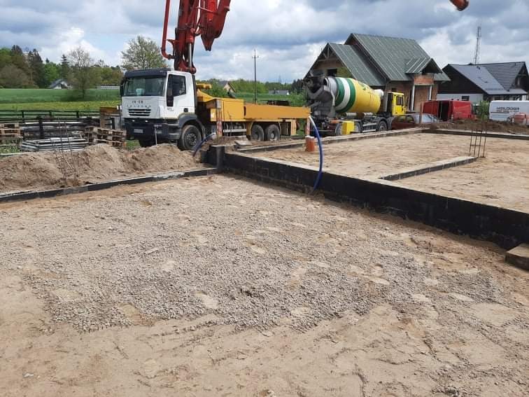 Przygotowanie terenu pod fundamenty w Egiertowie: widok na zbrojenie, szalunki, pompę do betonu i betoniarkę na tle budującego się domu.