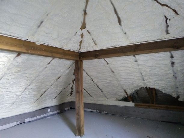 Poddasze z drewnianą konstrukcją krokwiową pokryte grubą warstwą białej pianki izolacyjnej, widoczne niedociągnięcia w aplikacji w górnej części dachu.