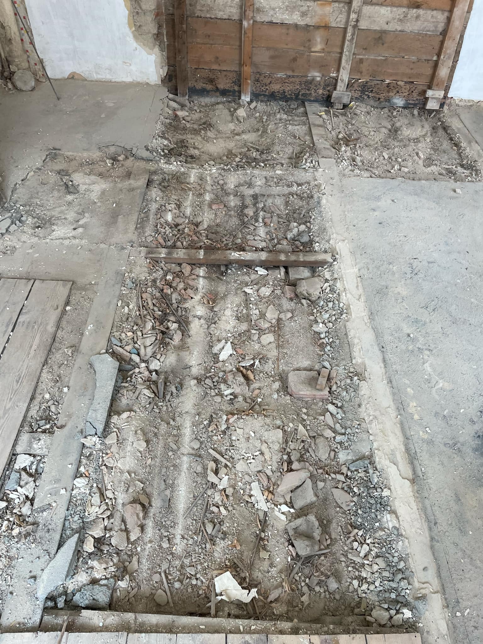 Fragment podłogi w trakcie remontu, z widocznymi usuniętymi deskami, gruzem i odsłoniętą konstrukcją drewnianą ściany.