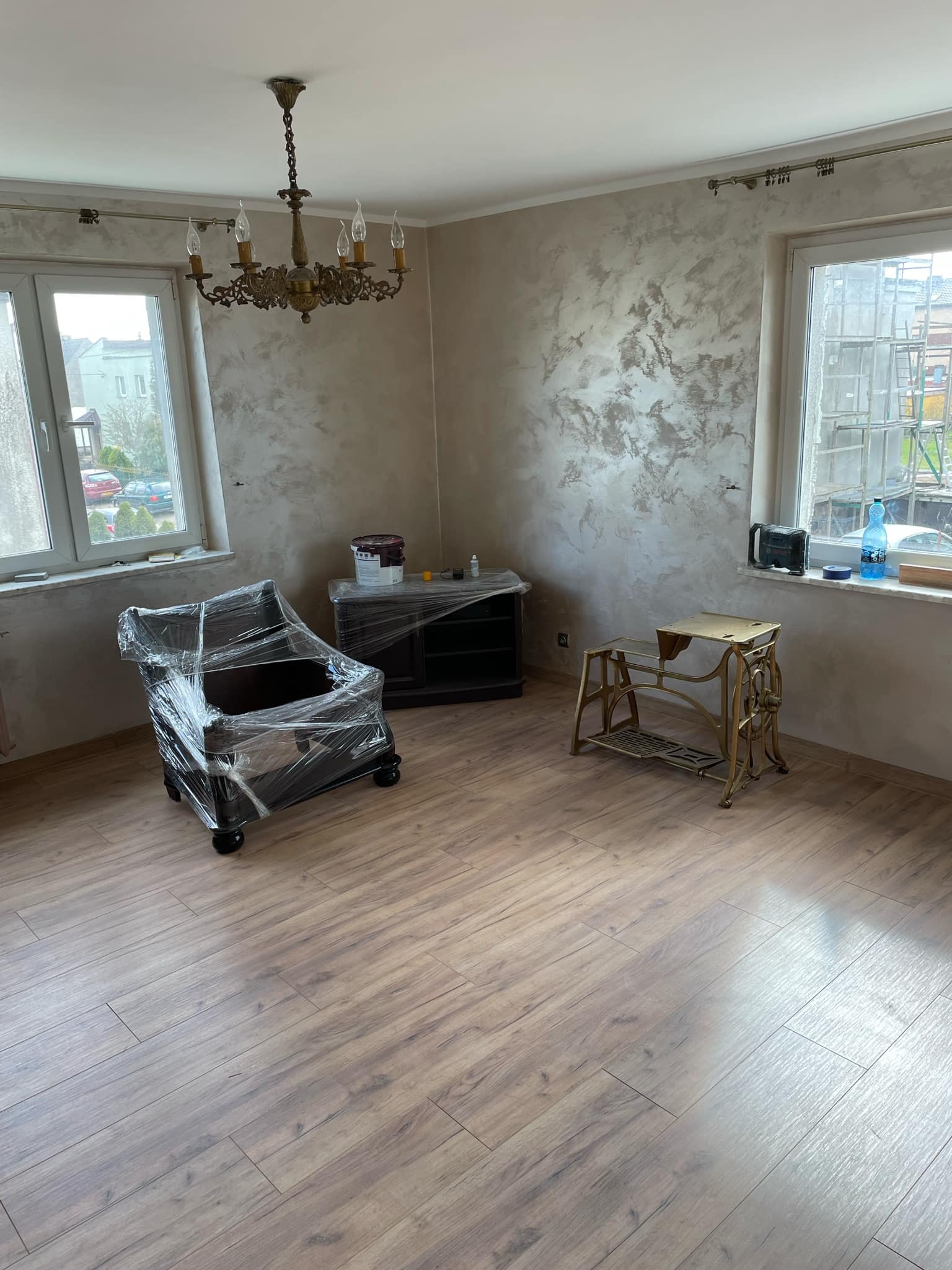 Pokój po malowaniu ścian z efektem dekoracyjnym, zabezpieczone folią meble, widoczna stara maszyna do szycia i parkiet.