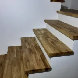 Nowoczesne, minimalistyczne schody drewniane z dębowymi stopniami zamontowanymi na białej ścianie, widziane od dołu pod kątem, ukazujące strukturę drewna.