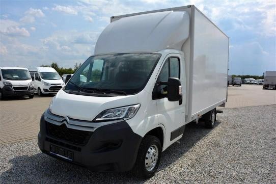 Biały samochód dostawczy Citroen Jumper z wysoką zabudową kontenerową na parkingu żwirowym, widoczne inne pojazdy w tle pod błękitnym niebem.