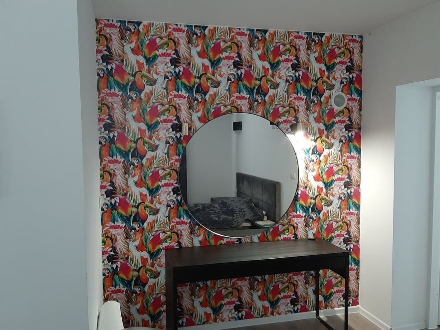 Ściana z tropikalną tapetą z motywem tukanów, okrągłe lustro i ciemna konsola w nowoczesnym wnętrzu sypialni.