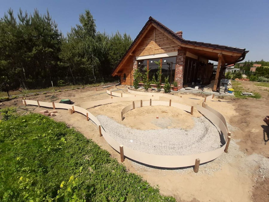 Przygotowanie terenu pod ścieżkę ogrodową z użyciem elastycznych obrzeży, widoczny dom z drewnianą elewacją i fragment ogrodu