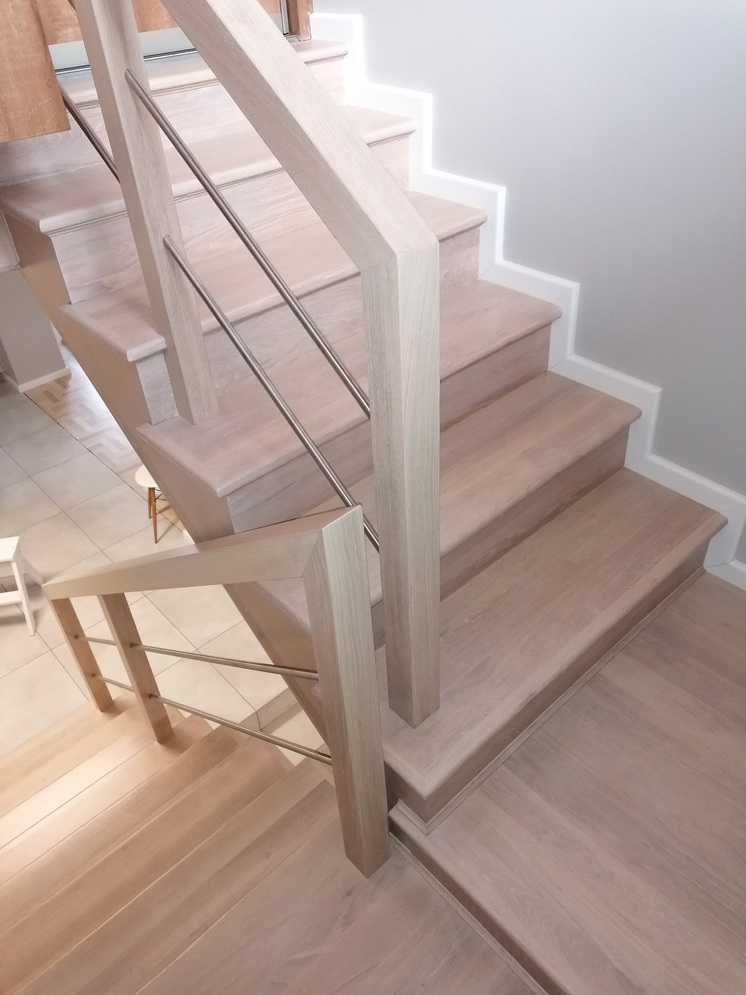 Jasne, drewniane schody z metalową balustradą i oświetleniem LED pod stopniami, widok z góry.