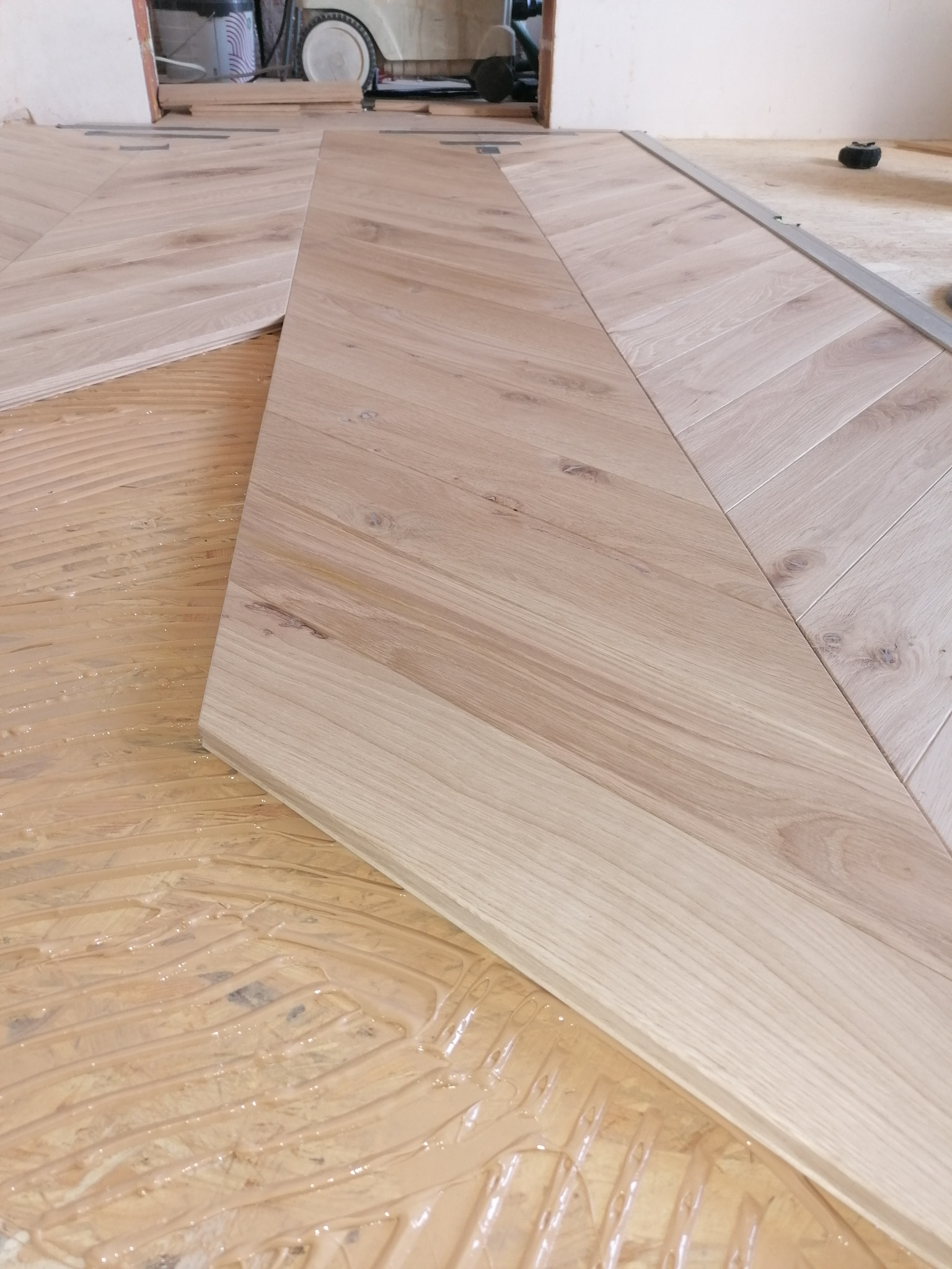 Fragment podłogi w trakcie montażu parkietu w jodełkę, widoczny klej i świeżo ułożone deski z jasnego drewna.