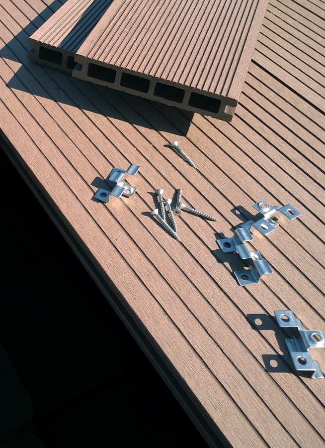Kompozytowe deski tarasowe, klipsy montażowe i wkręty na przygotowanym podłożu tarasu w słoneczny dzień.