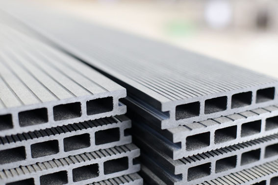 Szare deski kompozytowe tarasowe z rowkowaną powierzchnią, ułożone w stos z widocznymi prostokątnymi komorami powietrznymi.