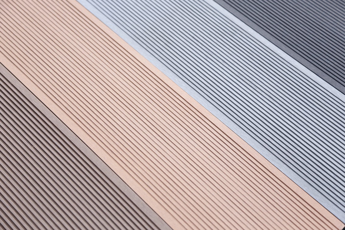 Kompozytowe deski tarasowe w odcieniach brązu, beżu, szarości i grafitu, ułożone diagonalnie, prezentujące fakturę ryflowaną.