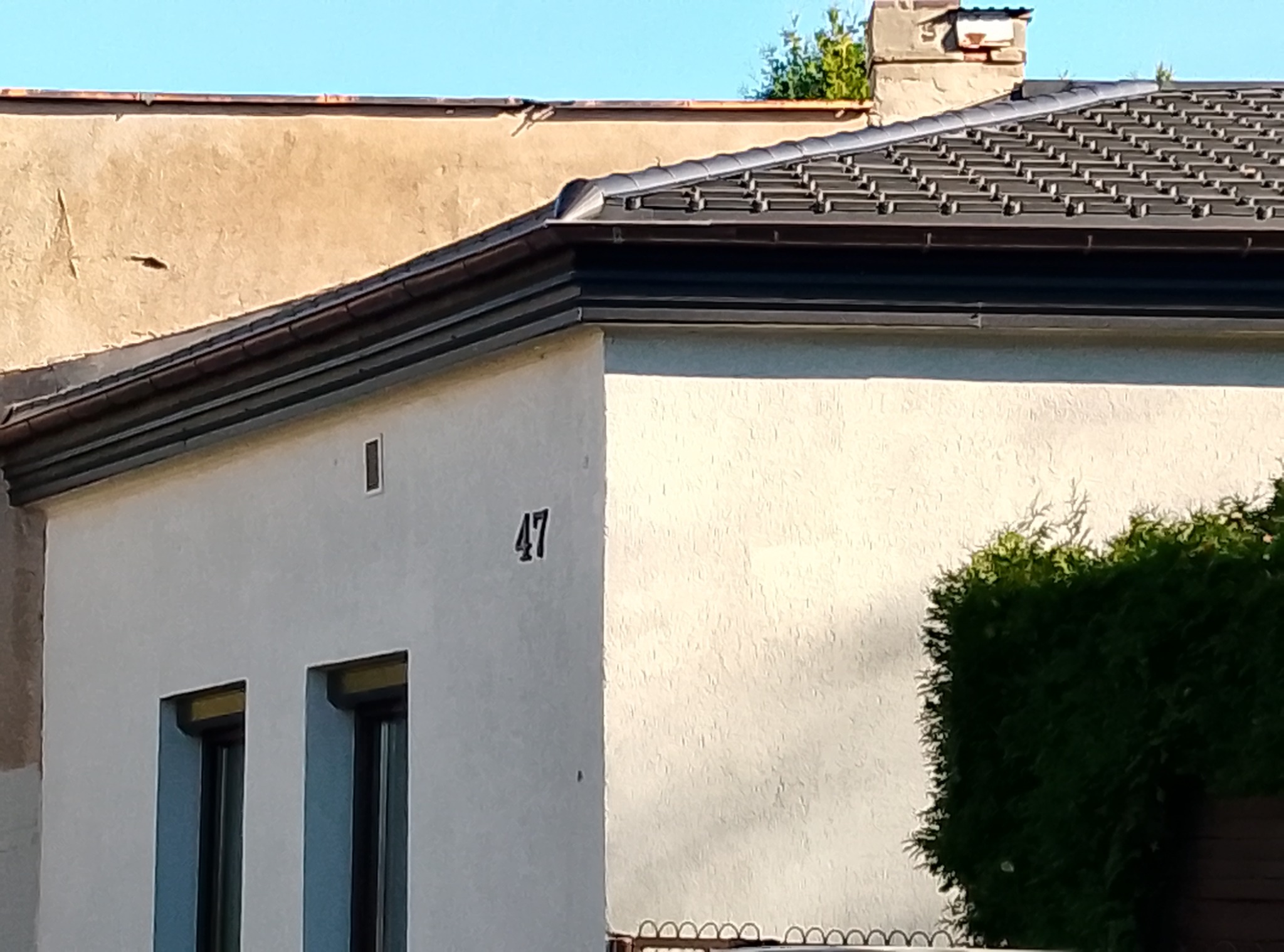 Dom z nowym, ciemnym dachem z dachówki ceramicznej, widoczny komin i numer domu '47'.
