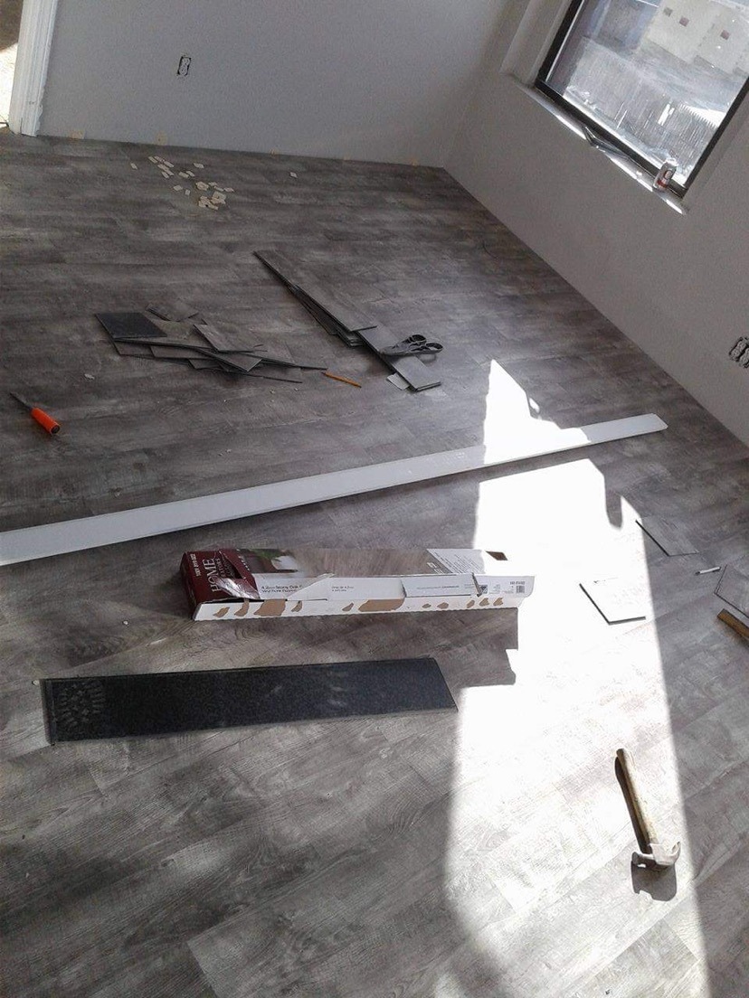 Układanie paneli podłogowych w trakcie remontu, widoczne panele, listwa przypodłogowa, narzędzia i pudełko po panelach w słonecznym pokoju.