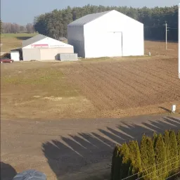 Widok z góry na białe hale namiotowe na polu, z widocznym zbiornikiem na wodę i drabinką w rogu kadru.