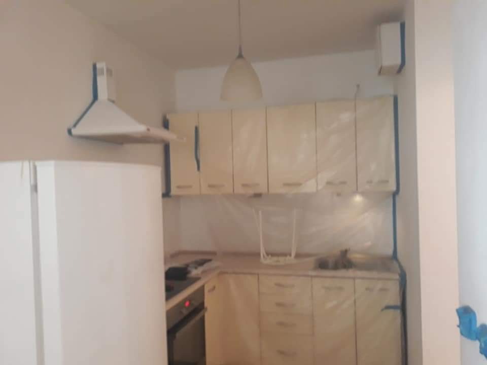 Kuchnia w trakcie zabezpieczania folią malarską przed pracami remontowymi, widoczny biały sprzęt AGD, beżowe szafki kuchenne i okap.