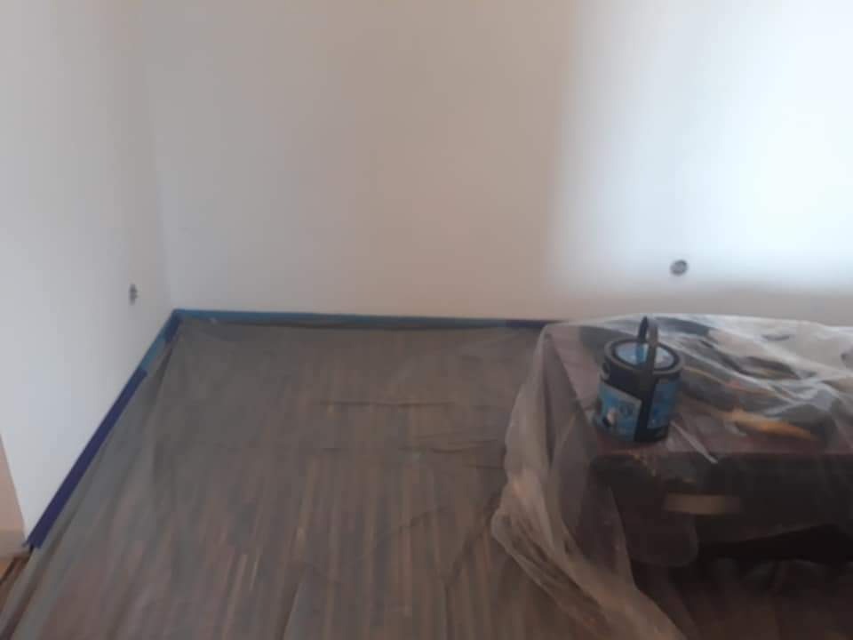 Przygotowanie do malowania: zabezpieczona folią podłoga i meble, puszka farby na stole, ściany przygotowane do malowania, zaklejone listwy przypodłogowe.