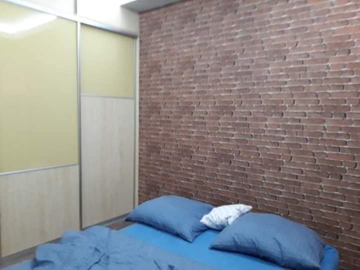 Sypialnia z łóżkiem w niebieskiej pościeli i ścianą wykończoną tapetą imitującą czerwoną cegłę, obok szafa przesuwna w jasnych kolorach.