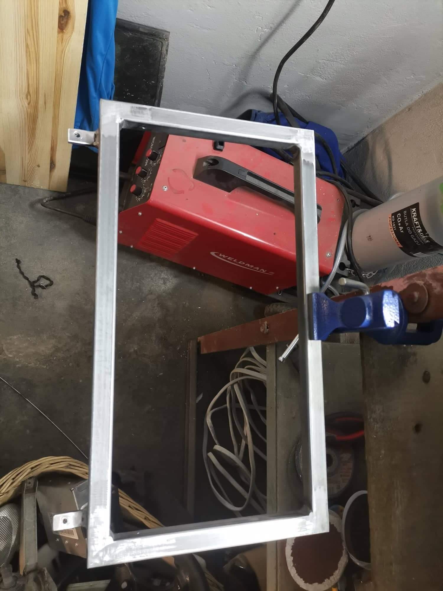 Spawana aluminiowa rama w uchwycie ślusarskim, widoczna spawarka Weldman i butla z gazem CO2+Ar w warsztacie w Mikołowie.