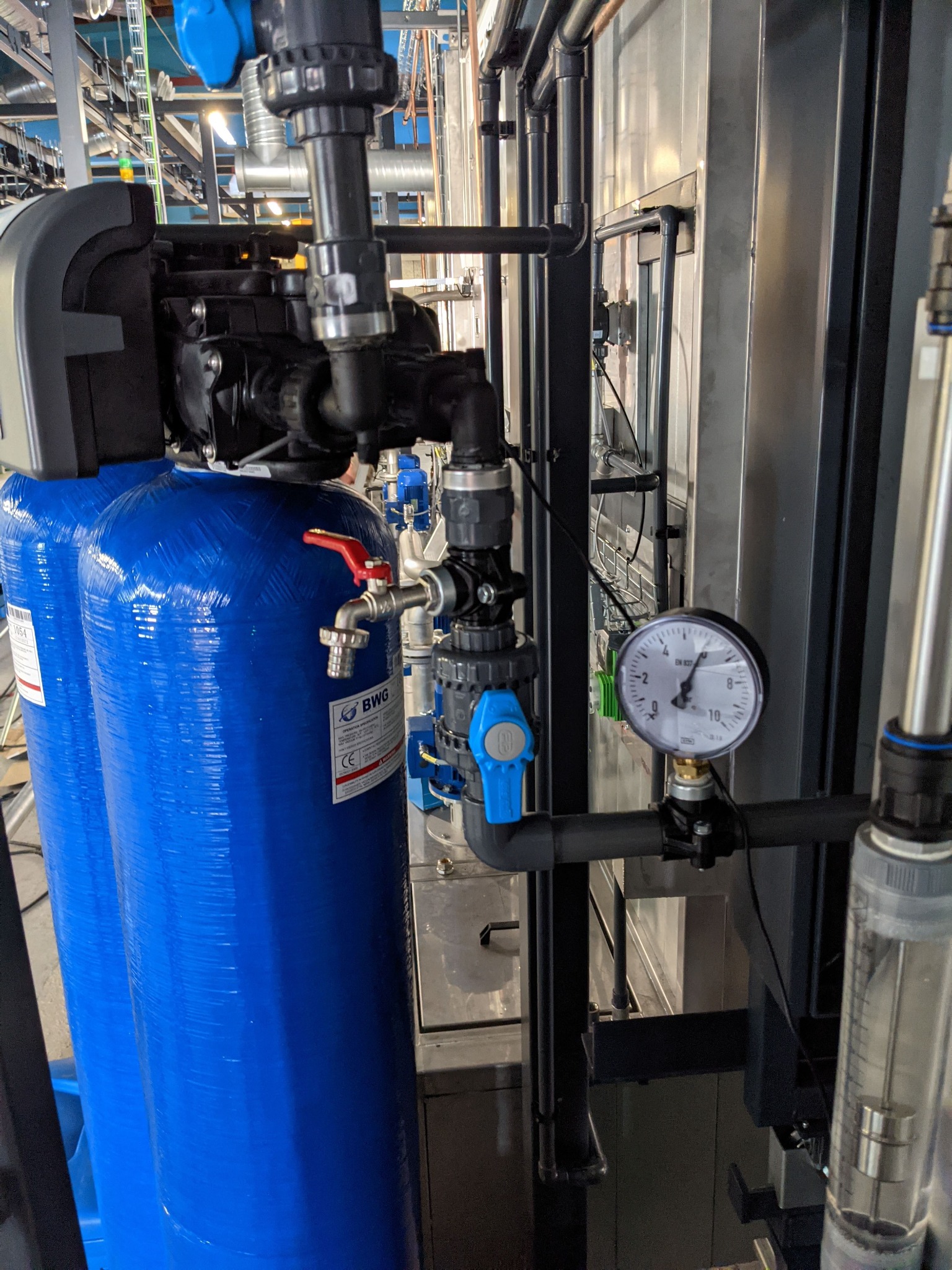 Dwa niebieskie zbiorniki ciśnieniowe z zaworami i manometrem w instalacji przemysłowej, widoczne rury i elementy złączne.