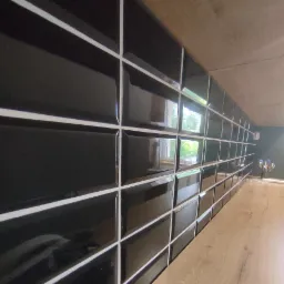 Błyszczące, czarne płytki ułożone na ścianie z wyraźną białą fugą, widok z perspektywy blatu.