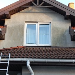 Daniel Dubis - Fragment elewacji domu z oknem i rynną, widoczna drabina oparta o dach. Ślady zabrudzeń na elewacji sugerują potrzebę odświeżenia.