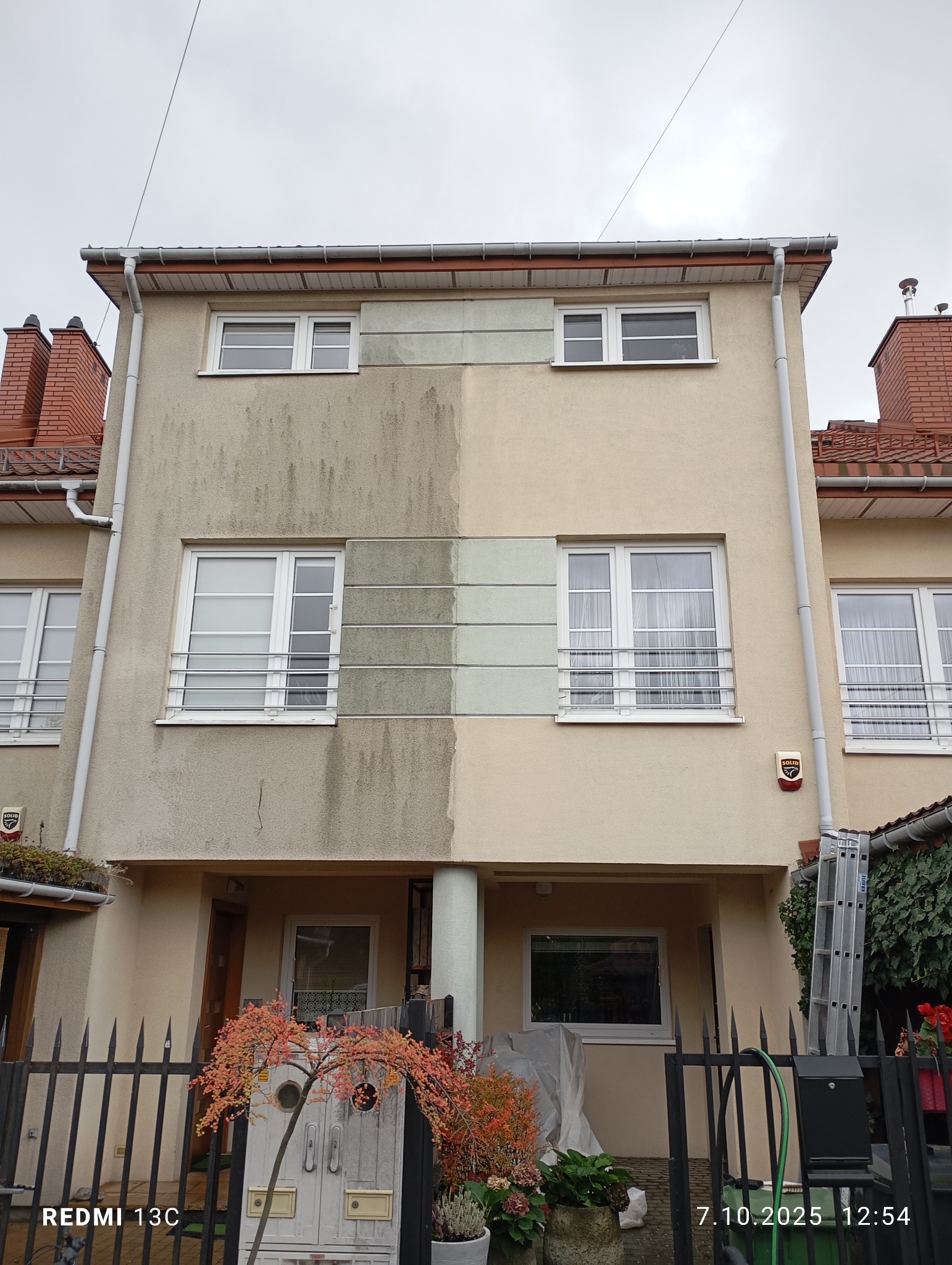 Dwukondygnacyjny dom z elewacją w połowie wyczyszczoną, ukazując różnicę przed i po zabiegu. Widoczne okna z kratami, rynny i fragment dachu z czerwonej dachówki.