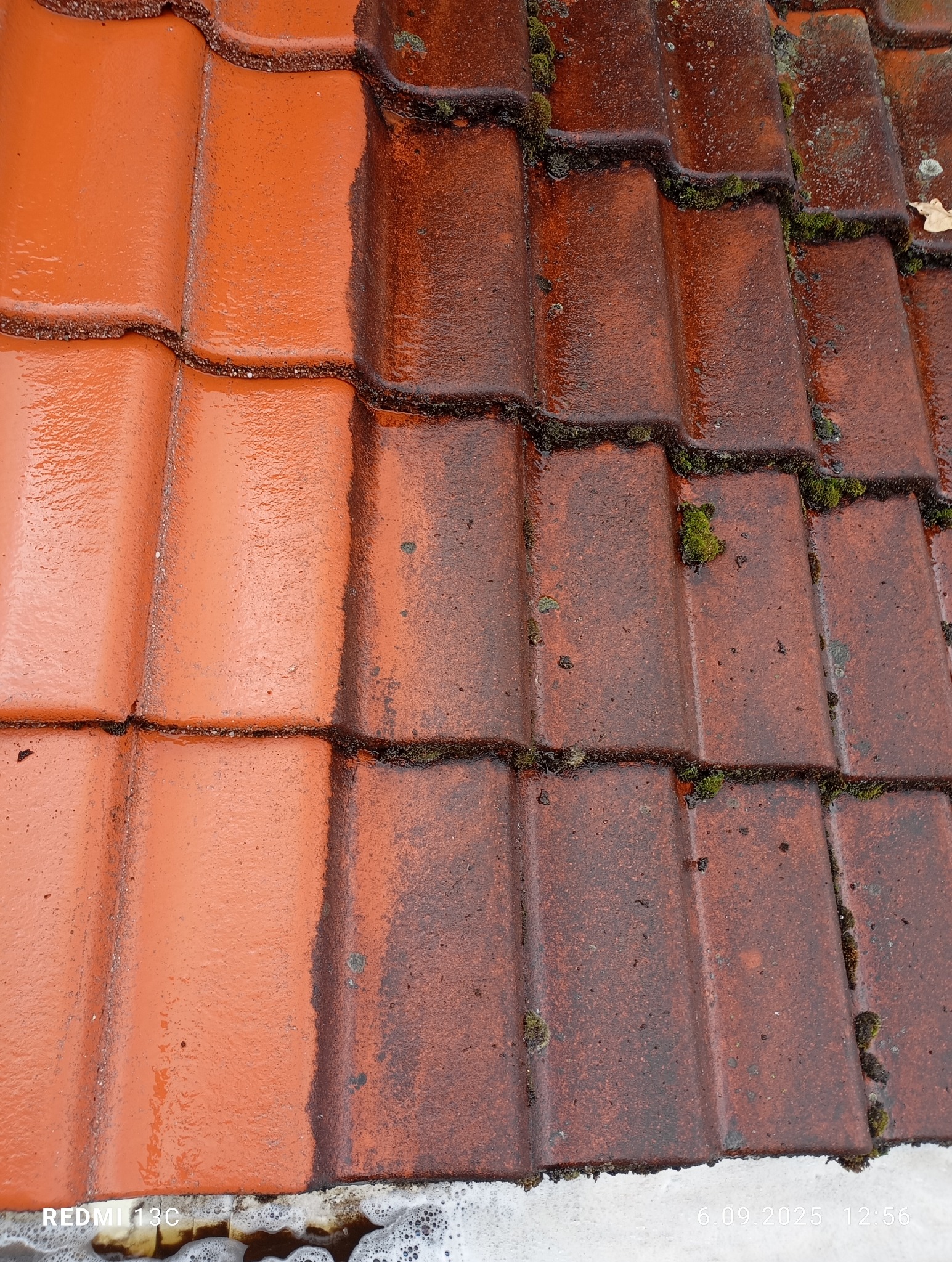 Częściowo umyta, czerwona dachówka z widocznym mchem i zabrudzeniami. Po lewej stronie dachówka czysta, po prawej brudna. Widoczne ślady wody i piany.