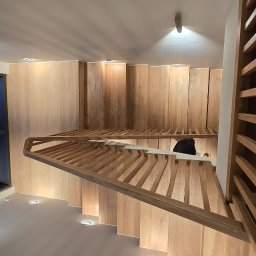 Stolarnia Rompa - Nowoczesne schody drewniane z podświetleniem LED wzdłuż stopni i ściany, widok z góry, z elementami ażurowej balustrady i dużym oknem z boku.