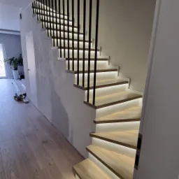 Nowoczesne schody z podświetlanymi stopniami i czarnymi, pionowymi balustradami, widok z dołu, drewniana podłoga.