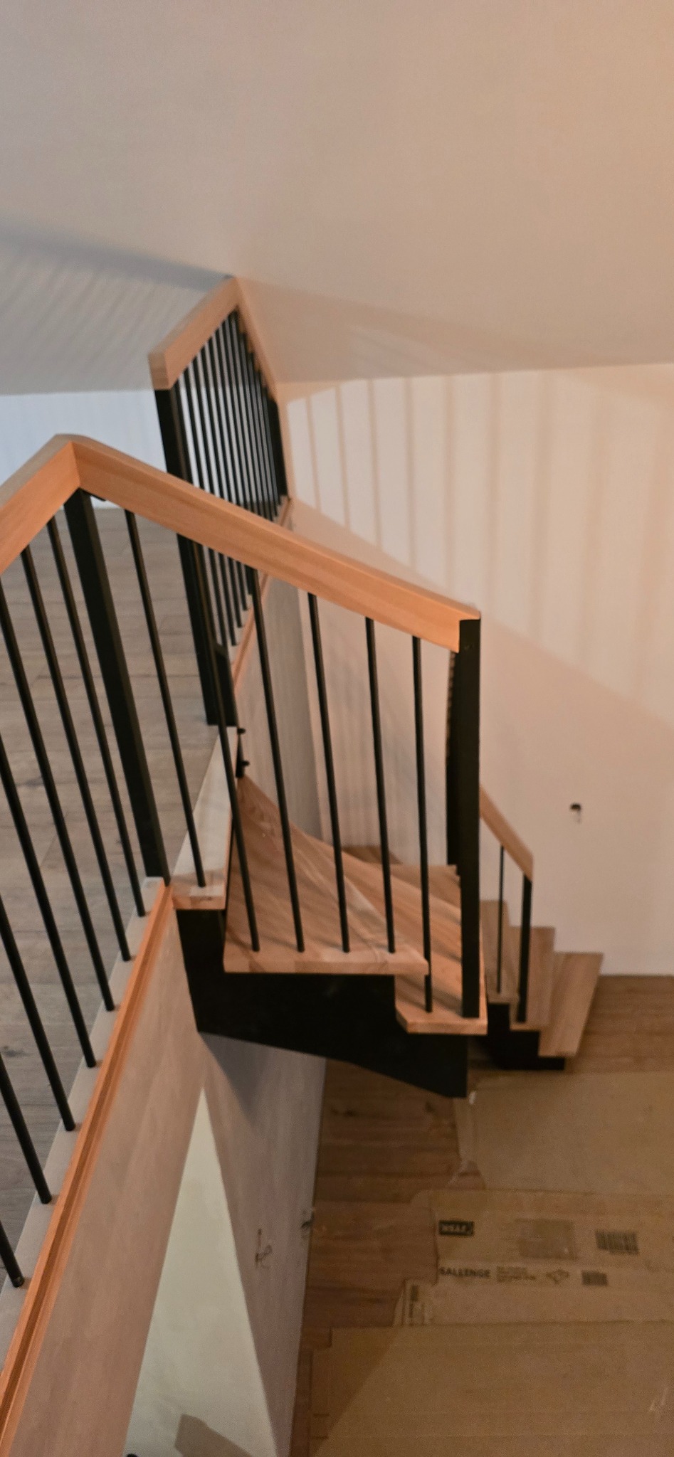 Nowoczesne schody z drewnianymi stopniami i czarnymi metalowymi balustradami, widok z góry, jasne wnętrze, minimalistyczny design.