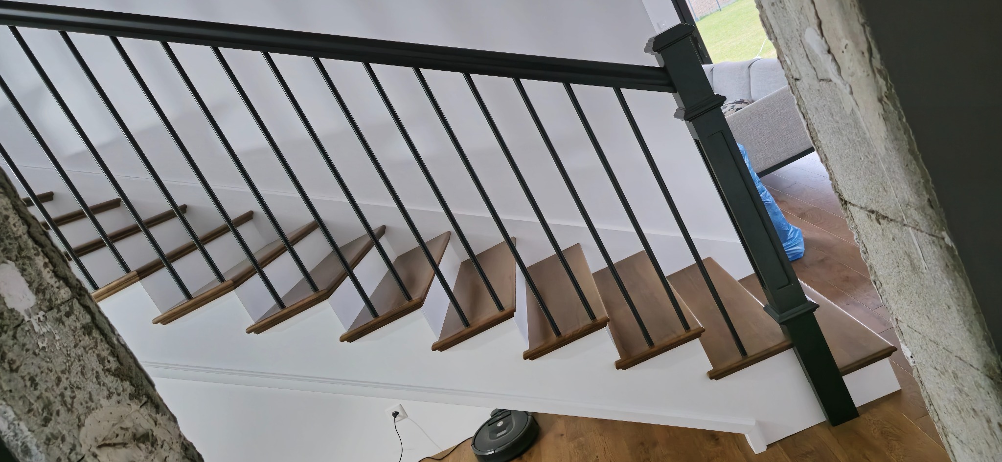 Nowoczesne schody z drewnianymi stopniami i czarną metalową balustradą, widok z góry, z robotem sprzątającym na podłodze. Minimalistyczny design.