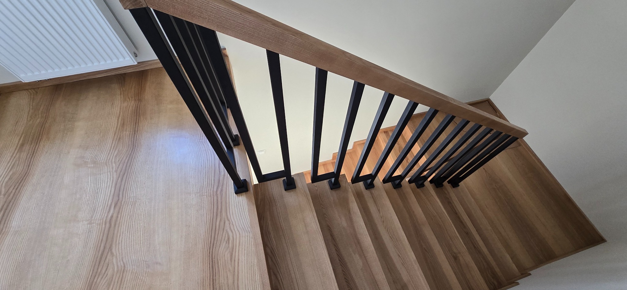 Nowoczesne schody z drewnianymi stopniami i czarną, metalową balustradą, widziane z góry. Realizacja z Parchowa. Jasne drewno, minimalistyczny design.