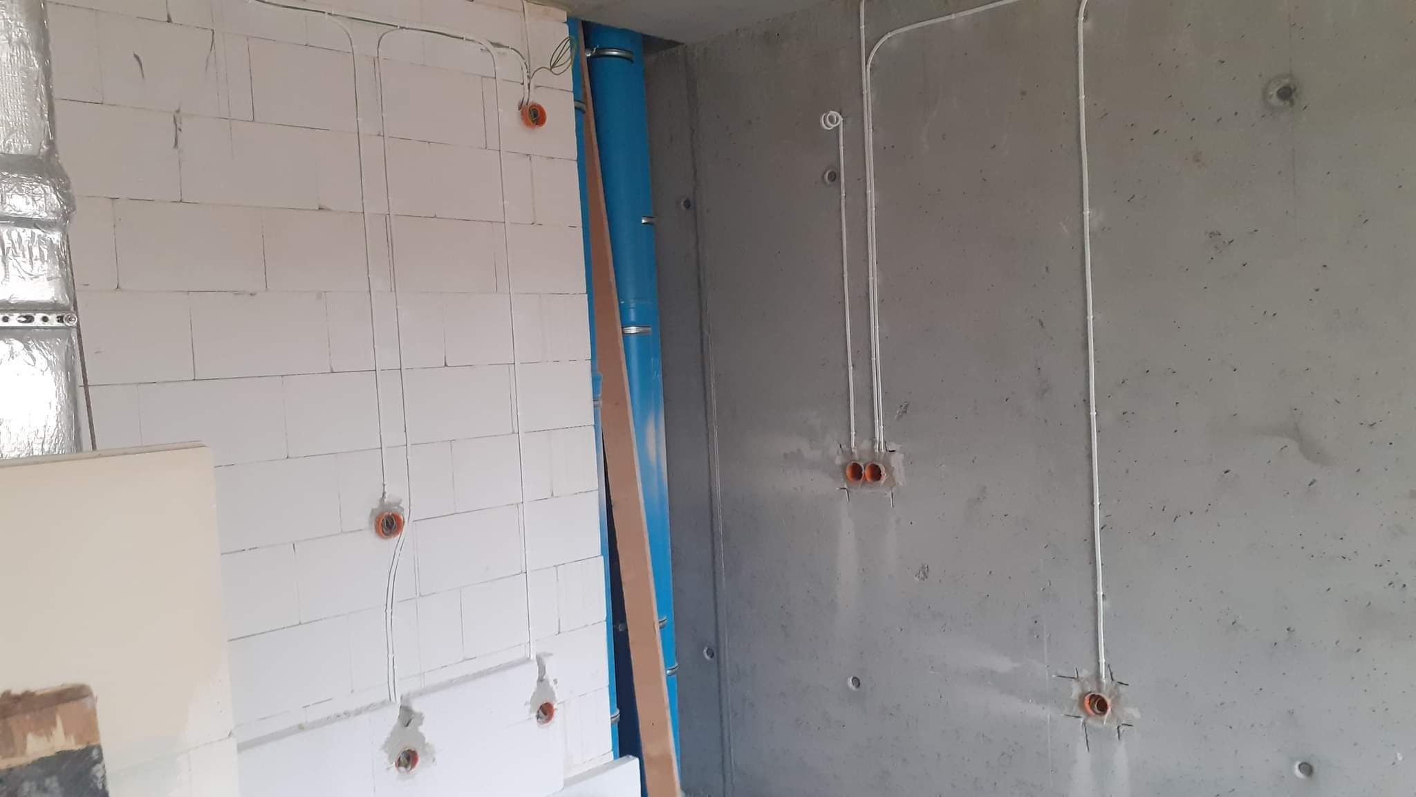 Surowy stan: przewody elektryczne w peszlach prowadzone po ścianach z betonu komórkowego i surowego betonu, widoczne puszki instalacyjne.