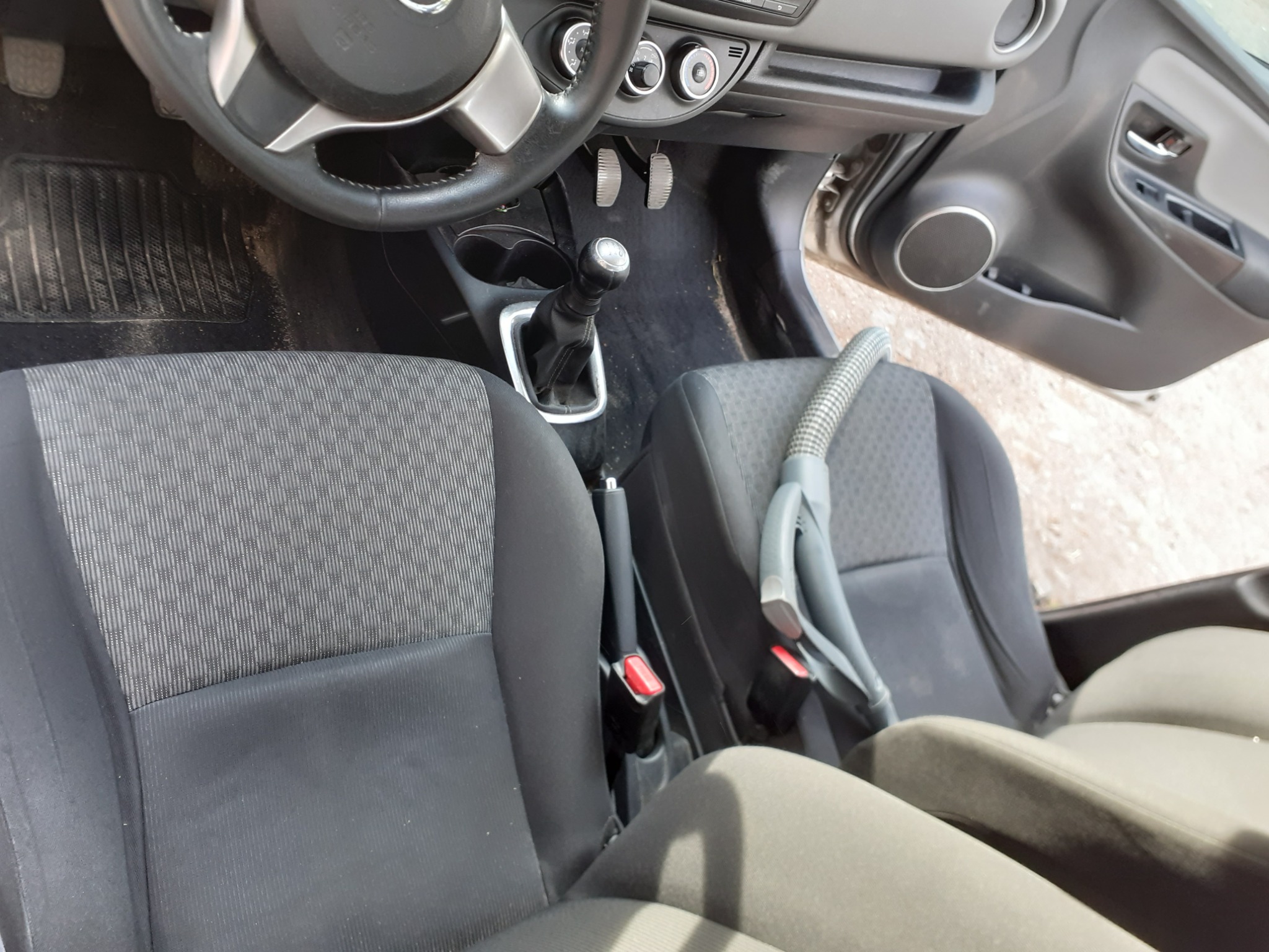 Wnętrze samochodu osobowego z widocznymi szarymi fotelami i dyszą odkurzacza leżącą na siedzeniu pasażera, sugerującą czyszczenie tapicerki.