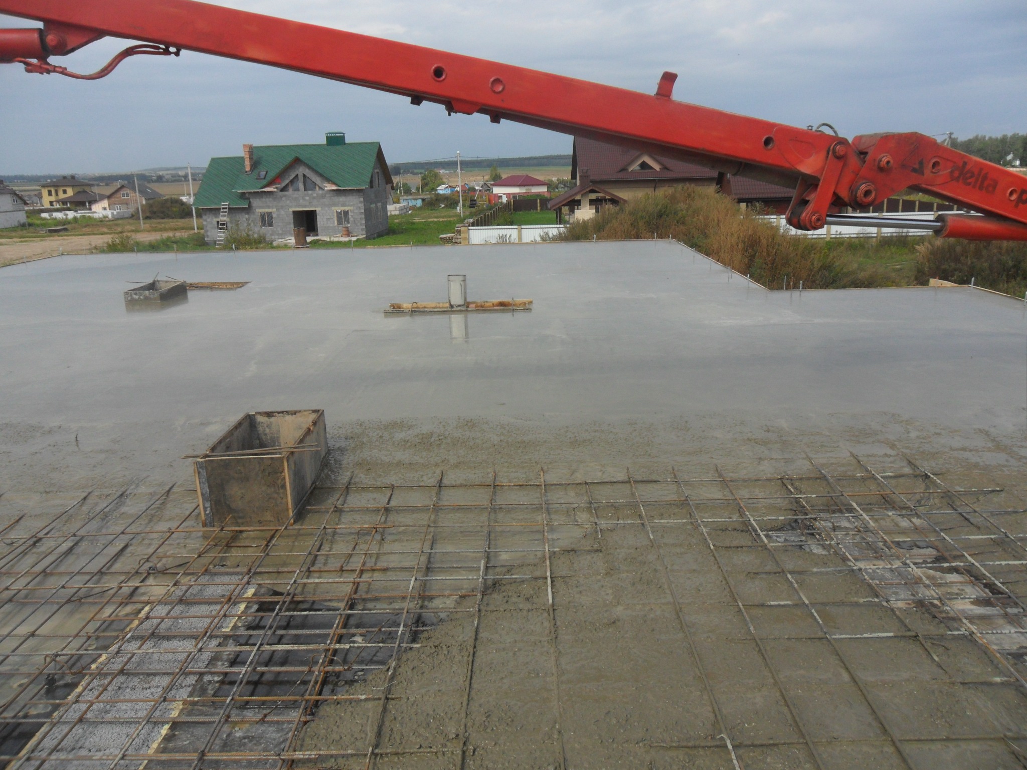 Wylewanie fundamentów domu jednorodzinnego w Warszawie, widoczna stalowa siatka zbrojeniowa i ramię pompy do betonu.