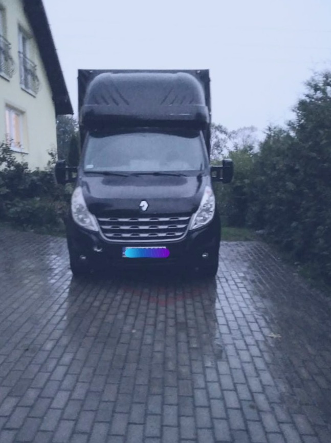 Czarny bus z wysoką zabudową stoi na brukowanym podjeździe przed domem w pochmurny dzień.