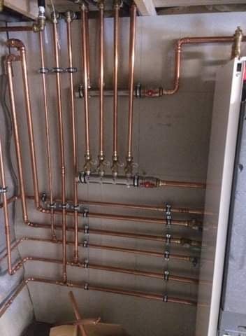 Miedziane rury instalacji centralnego ogrzewania z zaworami, zamocowane do ściany, widoczne elementy kotła.