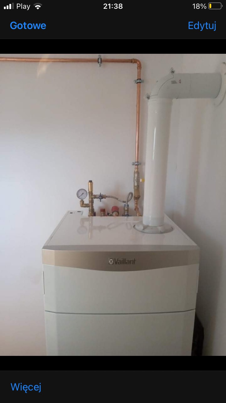 Biały, wiszący piec gazowy marki Vaillant z podłączonymi miedzianymi rurami i białym kominem, zamontowany na białej ścianie.