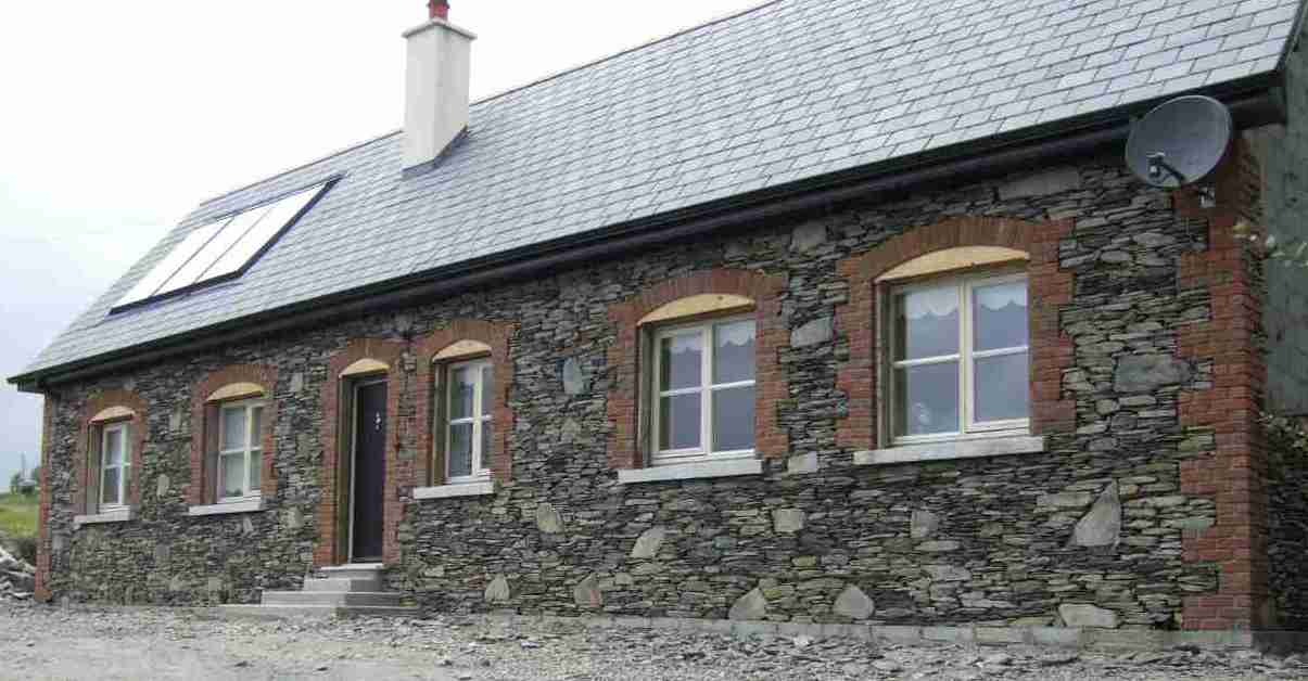 Dom z elewacją z łupka kamiennego, z ceglanymi obramowaniami okien i solarem na dachu, zwieńczony satelitarną anteną.