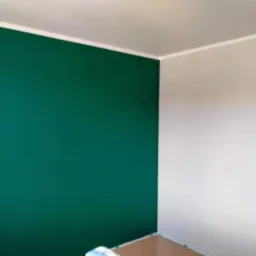 Pomieszczenie po malowaniu: jedna ściana w odcieniu butelkowej zieleni, druga biała, widoczne zabezpieczenia podłogi.