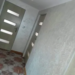 Korytarz po remoncie z dekoracyjną strukturą na ścianie, widoczne dwie pary drzwi z przeszkleniami i wzorzysta podłoga z płytek.