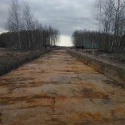 Przygotowany teren pod budowę drogi, widoczne wytyczone krawędzie i wyrównana powierzchnia gruntu, drzewa w tle.